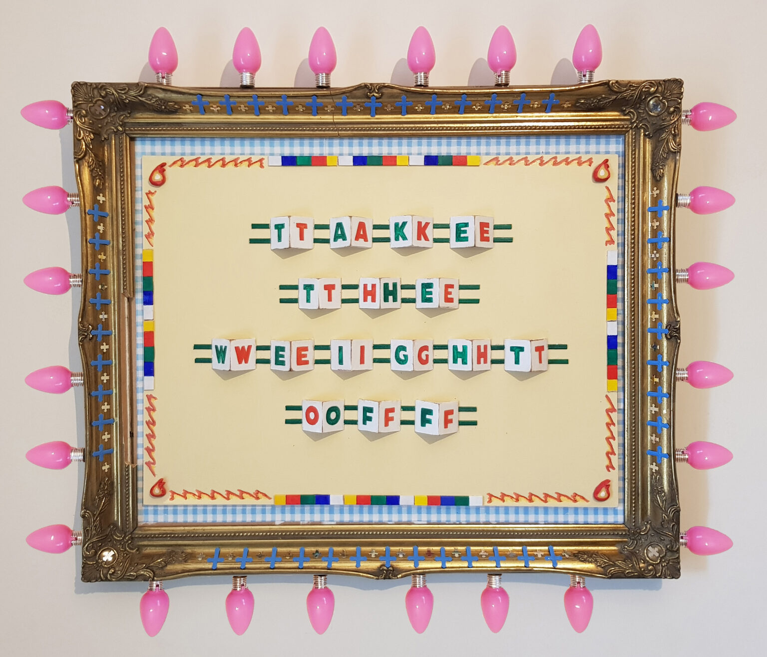 A photograph of a vibrant and energetic, non-traditional framed wall artwork. Inside the frame is text laid out across parallel green lines on a pale yellow background. In relief, each letter is drawn in in marker on white card, mirroring in two alternating colours of green and red, e.g. green T, red T, green A, red A… spelling out the phrase “Take The Weight Off”. One word per line, four lines in total. The artwork’s decorative border is made up of flame symbols, electric red lines and alternating colour blocks, all set on a base of gingham blue and white check. The gilt frame is decorated with rows of tiny blue and gold crosses, and extending from the four edges of the gilt frame are light bulbs in bubble-gum pink colour. The overall effect is one that is busy, visually exciting but somewhat overwhelming.